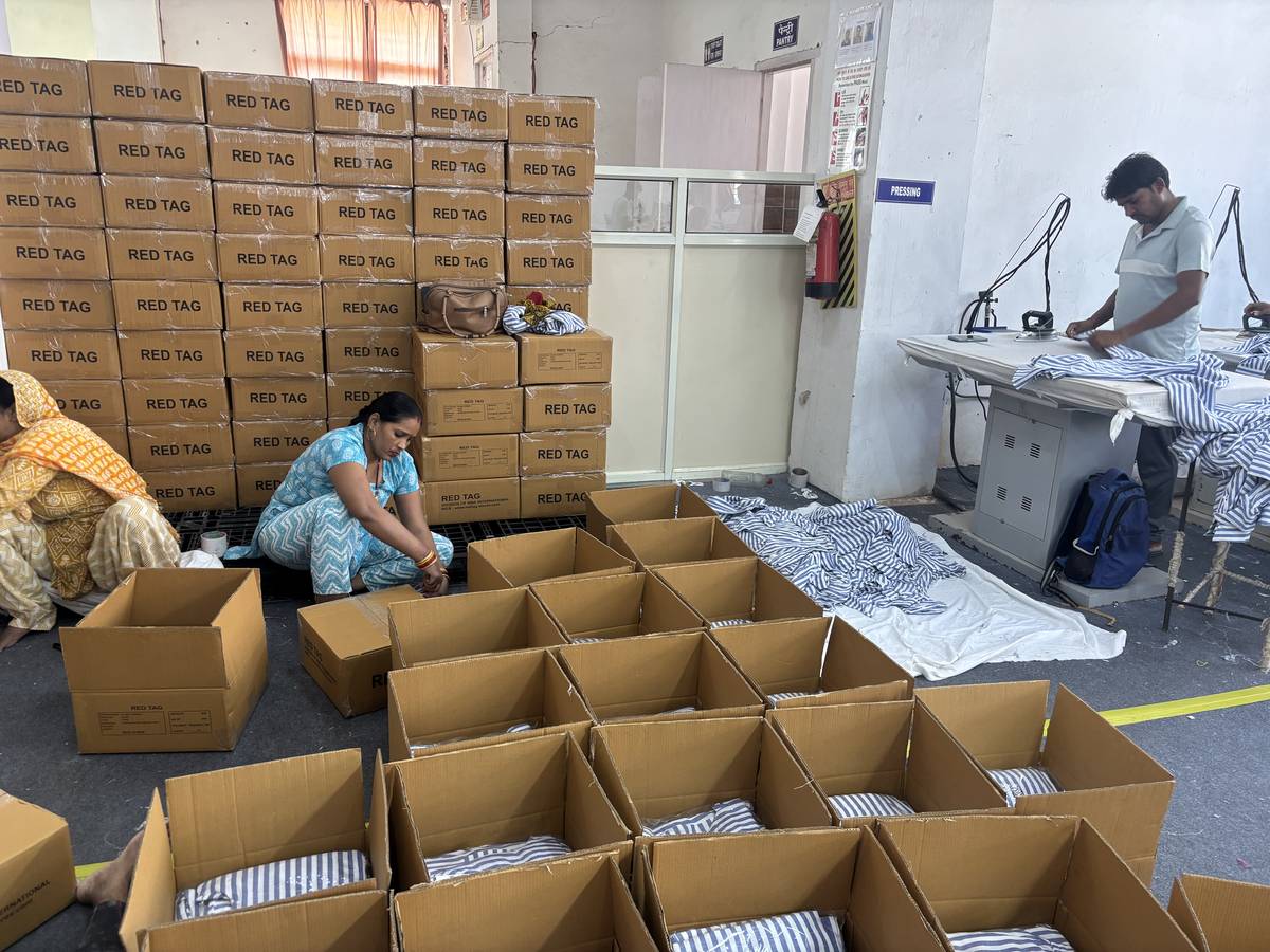 Workers packing finished striped shirts into export cartons beside the pressing station